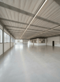 spacious room, white walls, concrete floor, large windows, metal beams, fluorescent lighting
