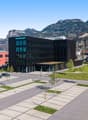 modern office building, green rooftop, parking lot, trees, cars parked, mountains in the background