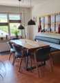 wooden dining table with 6 chairs, black bench with cushions, white wall, big windows, floor heating, plants