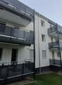 Modern apartment building with multiple balconies, white exterior, black railings, and a small garden in front.
