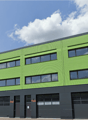 A multi-story commercial building with a green exterior and large windows. The building has multiple garage doors on the ground floor, indicating it may be used for industrial or warehouse purposes.