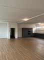 an empty, spacious room with wooden floors, white walls, and a kitchen area in the back