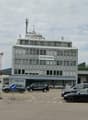 Multi-story office building with the Zurcher logo prominently displayed, surrounded by parked cars in a parking lot.