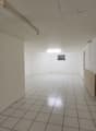 The image shows a large, empty room with white walls and a tiled floor. The room appears to be in a commercial or industrial building, with a simple light fixture visible on the ceiling.