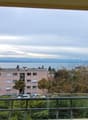 View from a balcony with a railing showing a cityscape with a lake in the background, surrounded by trees and buildings, with cars parked in front.