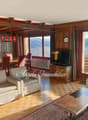 living room with wooden walls, wooden floor, large windows, dining table, sofa, armchairs, coffee table, television, rug, wooden cabinet