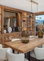 Dining room with wooden table, white chairs, wooden shelves, large windows, mountain view