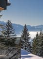 Glass wall, snow-covered mountains, pine trees, clear blue sky
