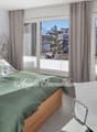 large bed, green linens, pillows, gray curtains, white walls, desk, chair, lamp, balcony, mountain view