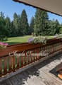 Wooden deck with railing, surrounded by lush greenery and flowers. Scenic view of the forest and open grassy area.
