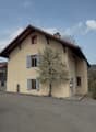 2 story house, beige walls, brown roof, windows with shutters, tree in front