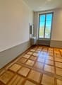 Empty room with wooden parquet flooring, white walls, a window, a small sink with a mirror, and a radiator.