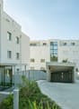 Multi-story apartment building with a garage entrance, glass windows, and landscaping around the entrance.