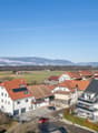 white building with red roof, balcony, solar panels on roof, mountains in the distance