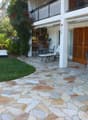 stone floored patio with dining table, chairs, 2 lounge chairs, balcony, shrubs and trees