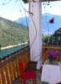Balcony with wooden railings, red chair, white table with flowers, red pillows, view of mountains and lake