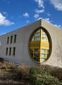 Modern building with a white brick facade, large yellow arched windows, and a circular window on the front.