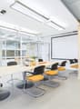 Modern office space with large conference table, yellow and black chairs, projector screen, and glass walls providing natural light