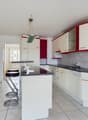 Spacious kitchen with white cabinets, red accents, granite countertops, tiled flooring, and a dishwasher. The kitchen is open to a dining area with a bar counter and stools.