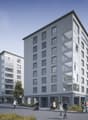 Modern apartment building with multiple floors, glass windows, balconies, and a flat roof.