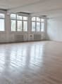 Empty room with large windows, wooden floor, white walls, built-in cabinets, radiators, fluorescent ceiling lights.