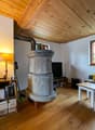 Cozy living room with wooden ceiling, stone fireplace, desk with computer, bookshelves, and a small table with chairs.