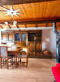 Rustic wooden interior with exposed beams, large wooden dining table and chairs, antique wooden cabinets, wood-burning stove, and decorative star-shaped light fixture
