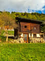 small wooden house, situated on a hill, surrounded by trees and grass, view of mountains