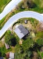 Aerial view of a house surrounded by lush green vegetation, with a winding road passing by the property.