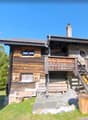 2-story wooden chalet-style house, with a balcony and porch, surrounded by trees and greenery