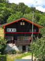 two story house, wooden exterior, slanted roof, wooden balcony, surrounded by plants