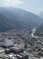Aerial view of a city with mountains in the background, large buildings, wide river, and trees and plants lining the streets.