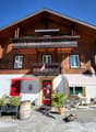 brown wooden exterior, red entrance, 2 balconies, flag, barrel in front