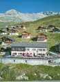 Collection of vacation houses, located on a hillside, surrounded by mountains, with an outdoor dining area.