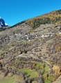 Mountain village, winding roads, mountainous landscape, green fields, snowy peaks, dense trees