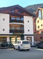 A three-story building with white and brown exterior, balconies on the second floor, and a name board 'TEA-ROOM ALETSCH'. There are several cars parked in front.