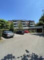 3-story brick apartment building with balconies, surrounded by trees, with a parking lot in the front