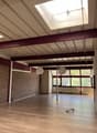 Empty room with brick wall, wooden floor, exposed ceiling beams, two large windows with white curtains, skylight, three hanging lamps