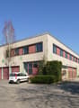 Industrial building with red garage doors, white car parked in front, large windows, green bushes, clear sky