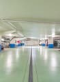 Underground parking lot with multiple cars parked, white and blue pillars, green floor, white ceiling, lights