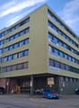 Multi-story office building, green exterior, several windows, parking area in front, staircases on side