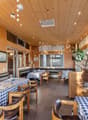 Cozy wooden interior with checkered tablecloths, leather seating, and nautical decor elements like a model ship. The space features pendant lighting, an air conditioning unit, and a dishwasher visible in the background.