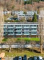 Apartment building with several floors, balconies, parking lot, green grass and many trees in the surroundings.