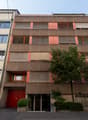 Modern multistory apartment building with multiple balconies, garage entrance, trees, and bicycle racks