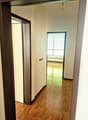 Hallway with hardwood floors, white walls, and a window with blinds. There are two doors leading to other rooms.