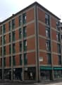 Multi-story residential building, brick walls, green shutters, air conditioning units on facade, ground floor shops, white walls