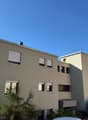Multi-storey apartment building, beige paint, multiple windows, chimney, greenery in front, mountain in the background