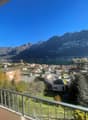 View from a balcony overlooking a village with mountain range, lake, and sky.