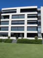 Multi-story apartment building, white exterior with glass balconies, greenery, modern design, large grassy lawn