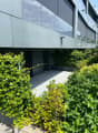 Modern apartment building, metallic facade, glass windows, greenery in the front